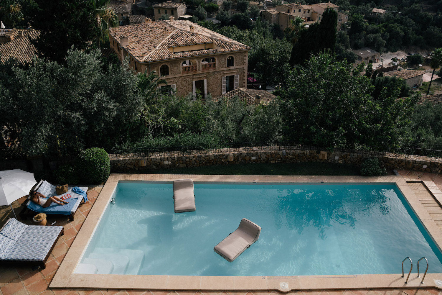 Two tan luxury pool float loungers shot from a distance in a swimming pool at the Belmond Hotel La Residencia in Mallorca.