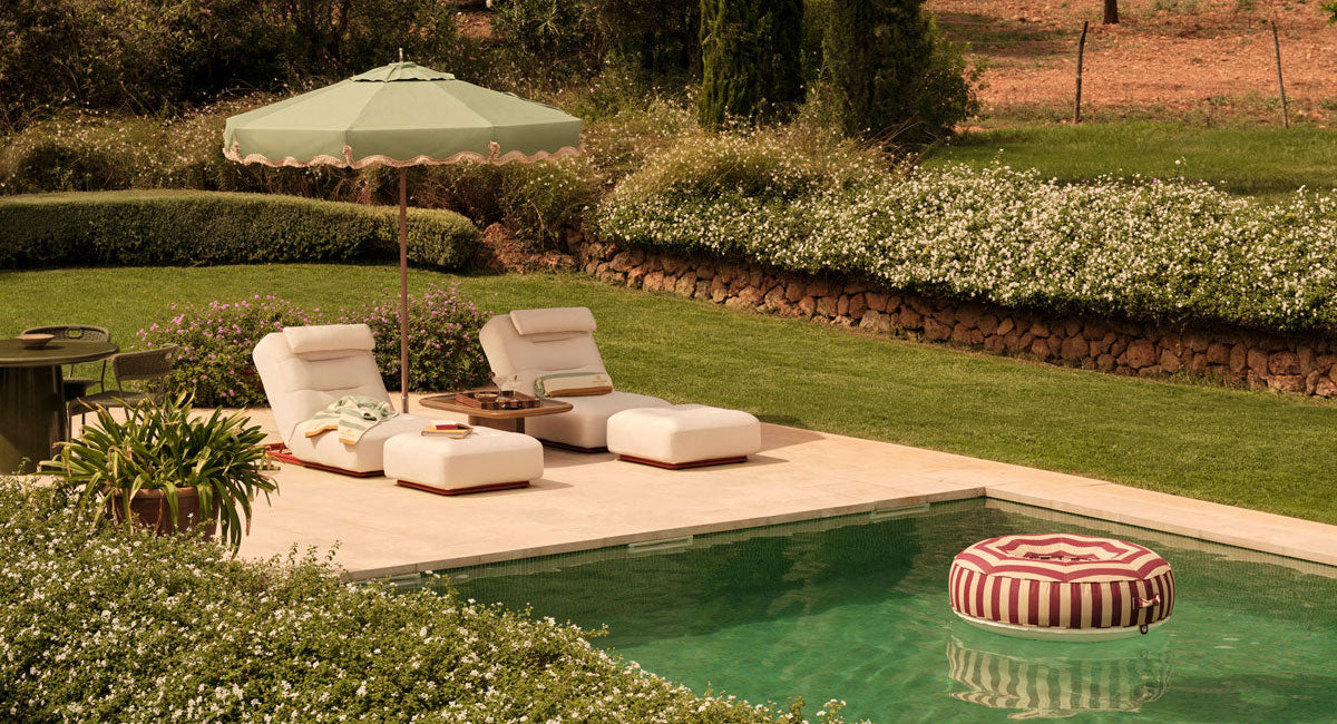 A red and white luxury pool float floating in a pool next to two luxury sun loungers.