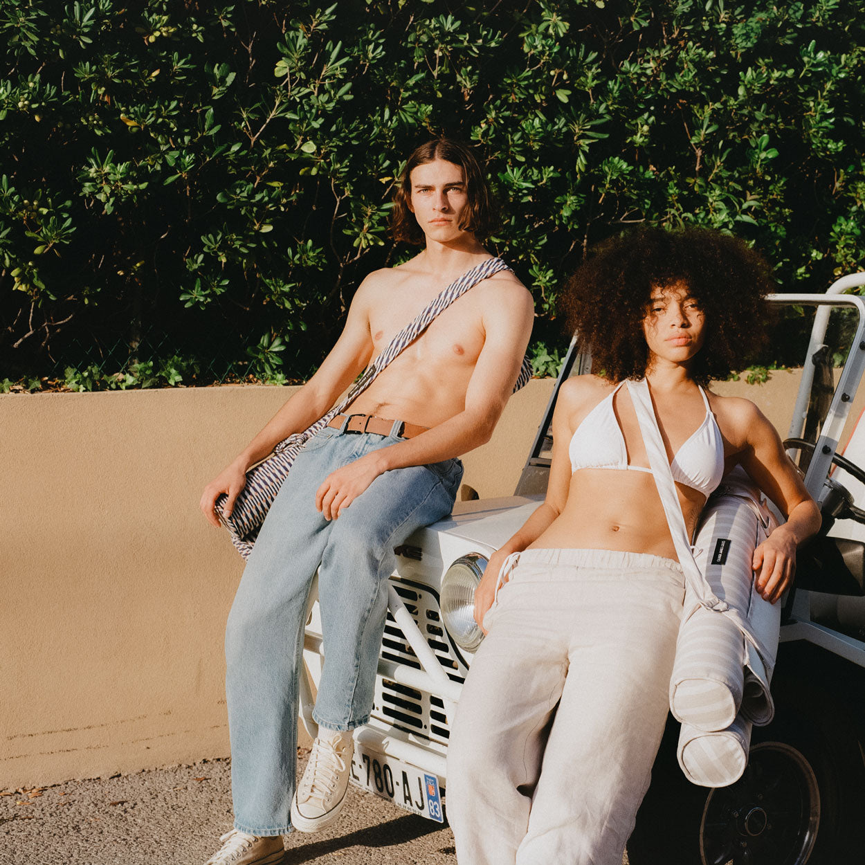 Two pool floats for adults strapped over models shoulders sitting on a vintage beach car.