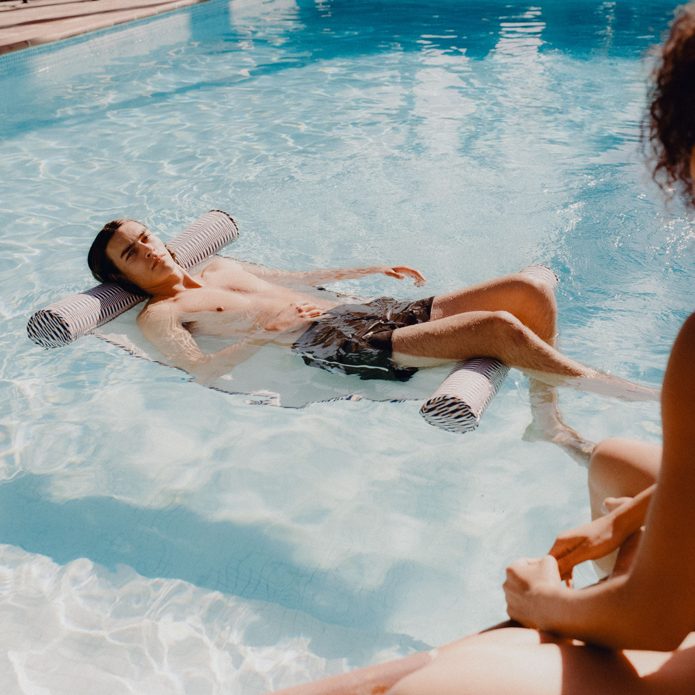 A pool toy for adults floating in a swimming pool with a man relaxing on it.