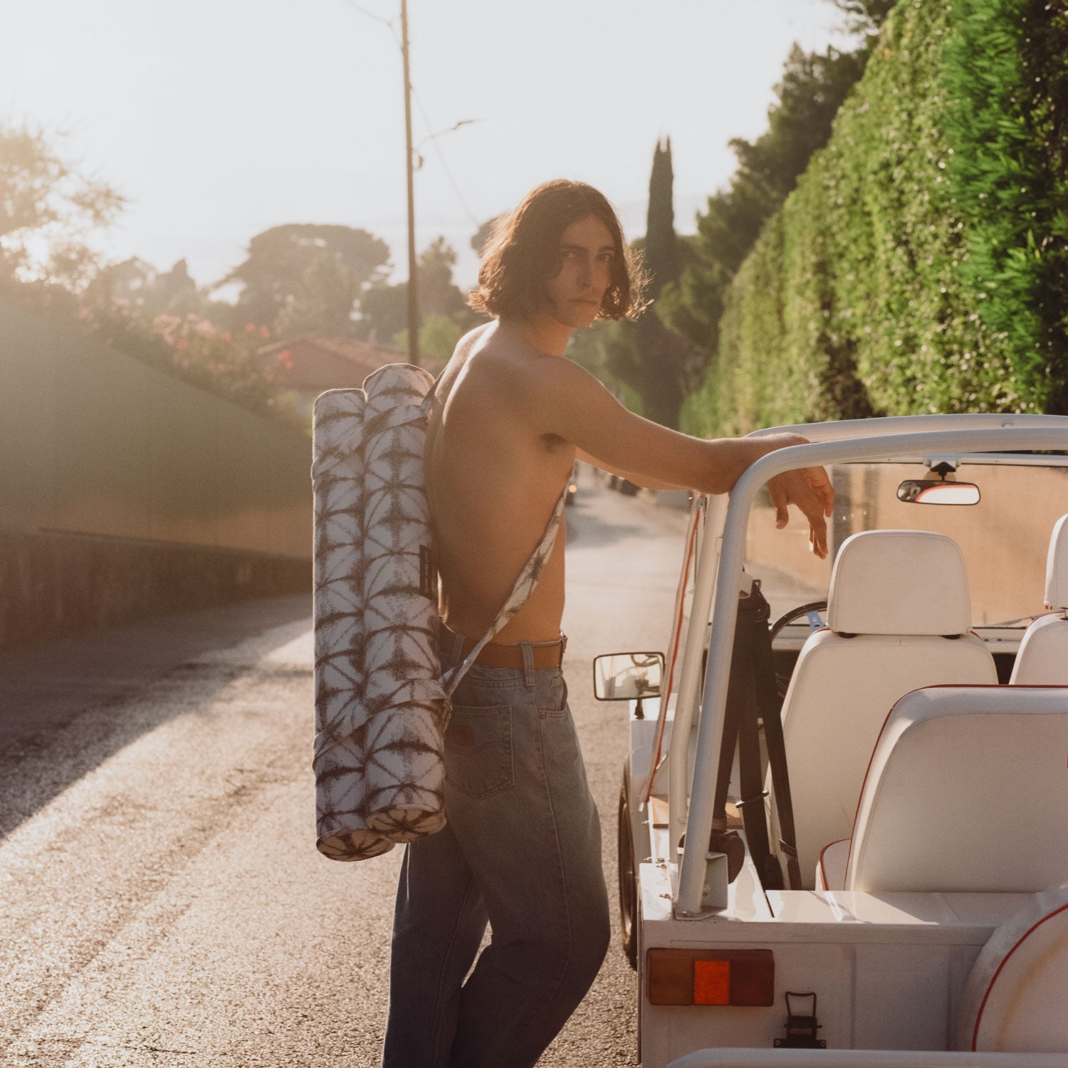 A man leaning against a vintage white car with a pool toy for adults strapped on his back.