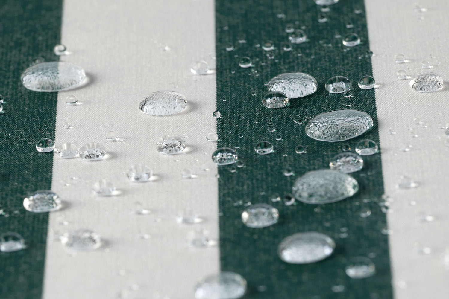 A waterproof outdoor fabric in a green and white bar stripe with several water droplets in frame.