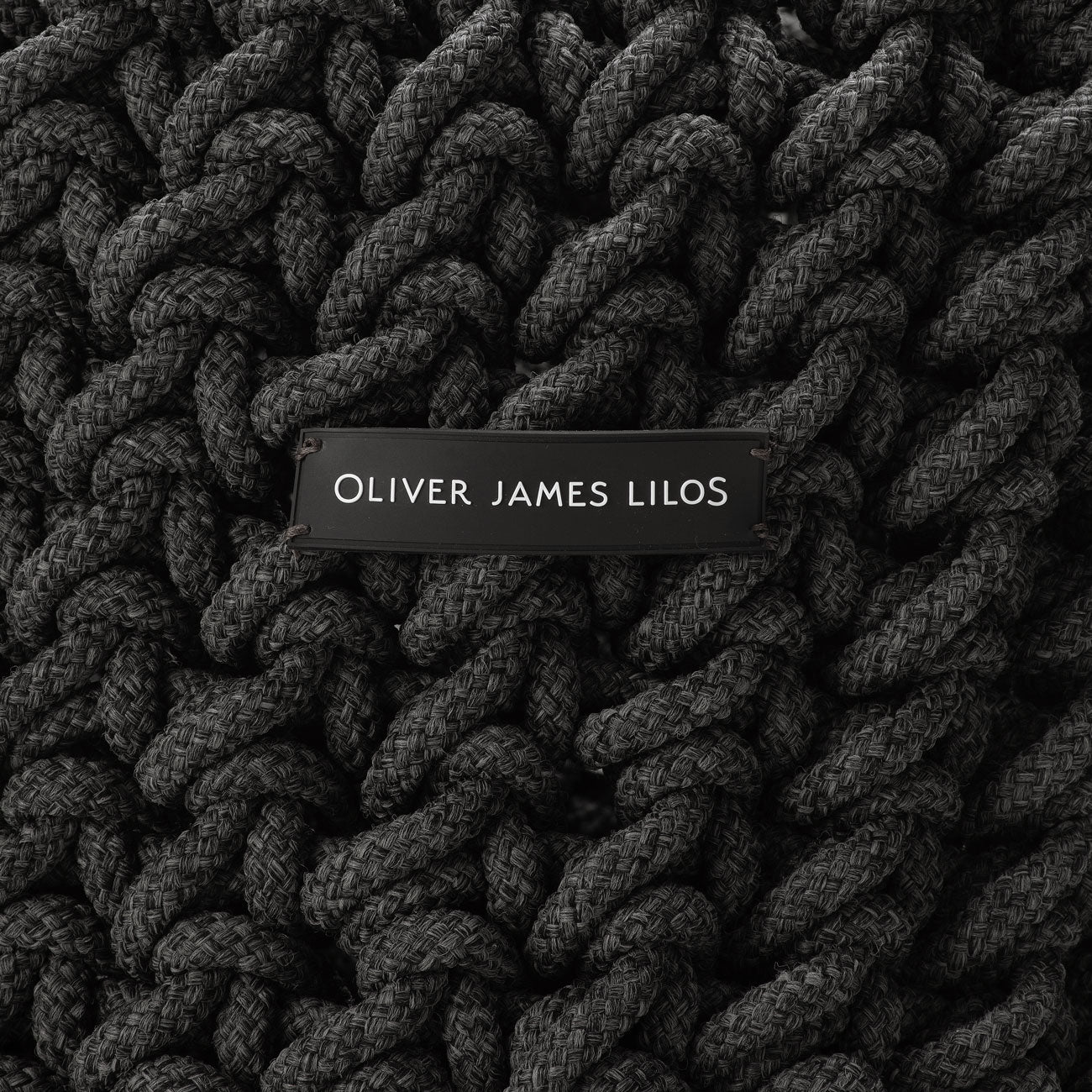 A hand-woven black rope basket with the logo "Oliver James Lilos".