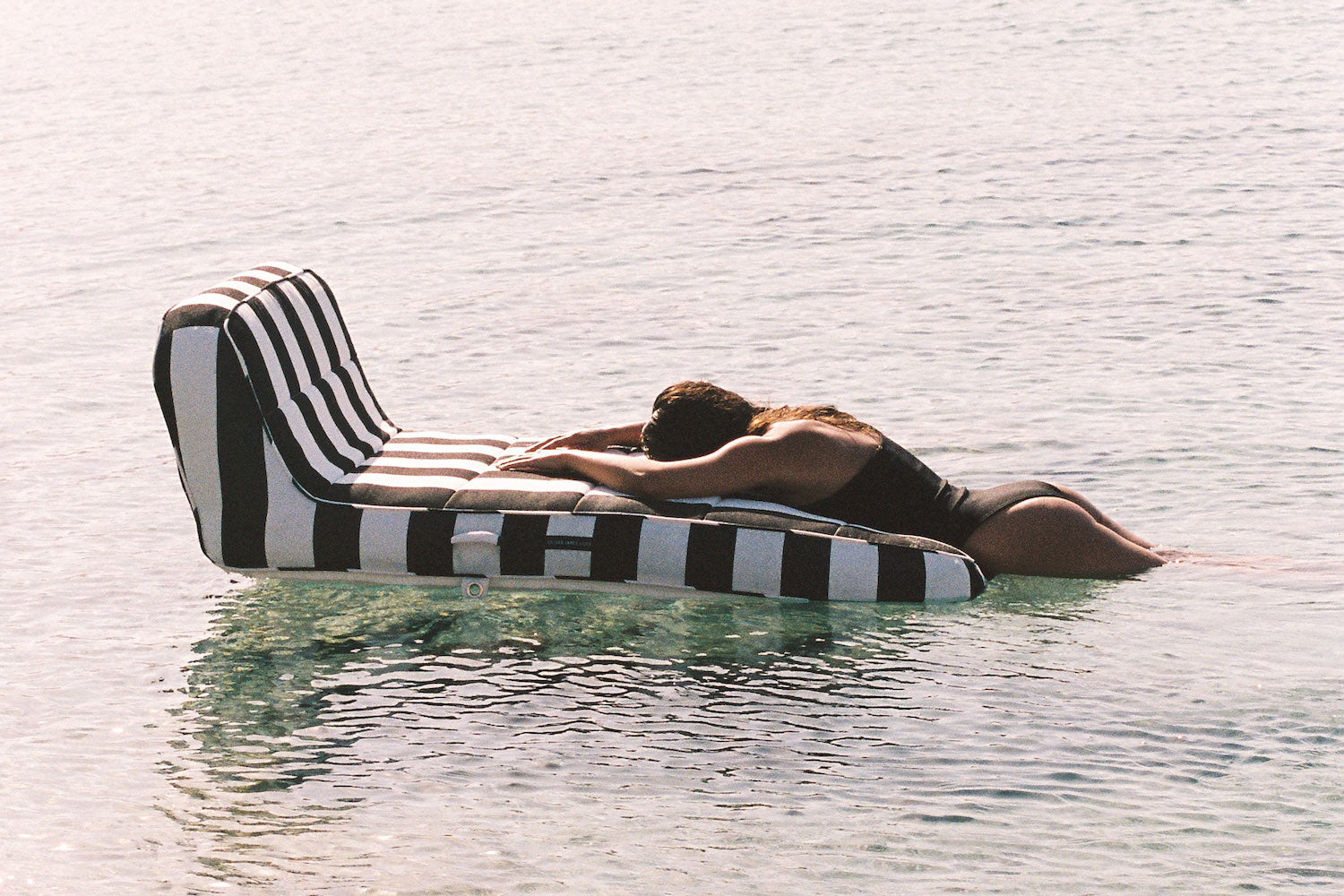 A woman lying on the end of a luxury pool float in the ocean.