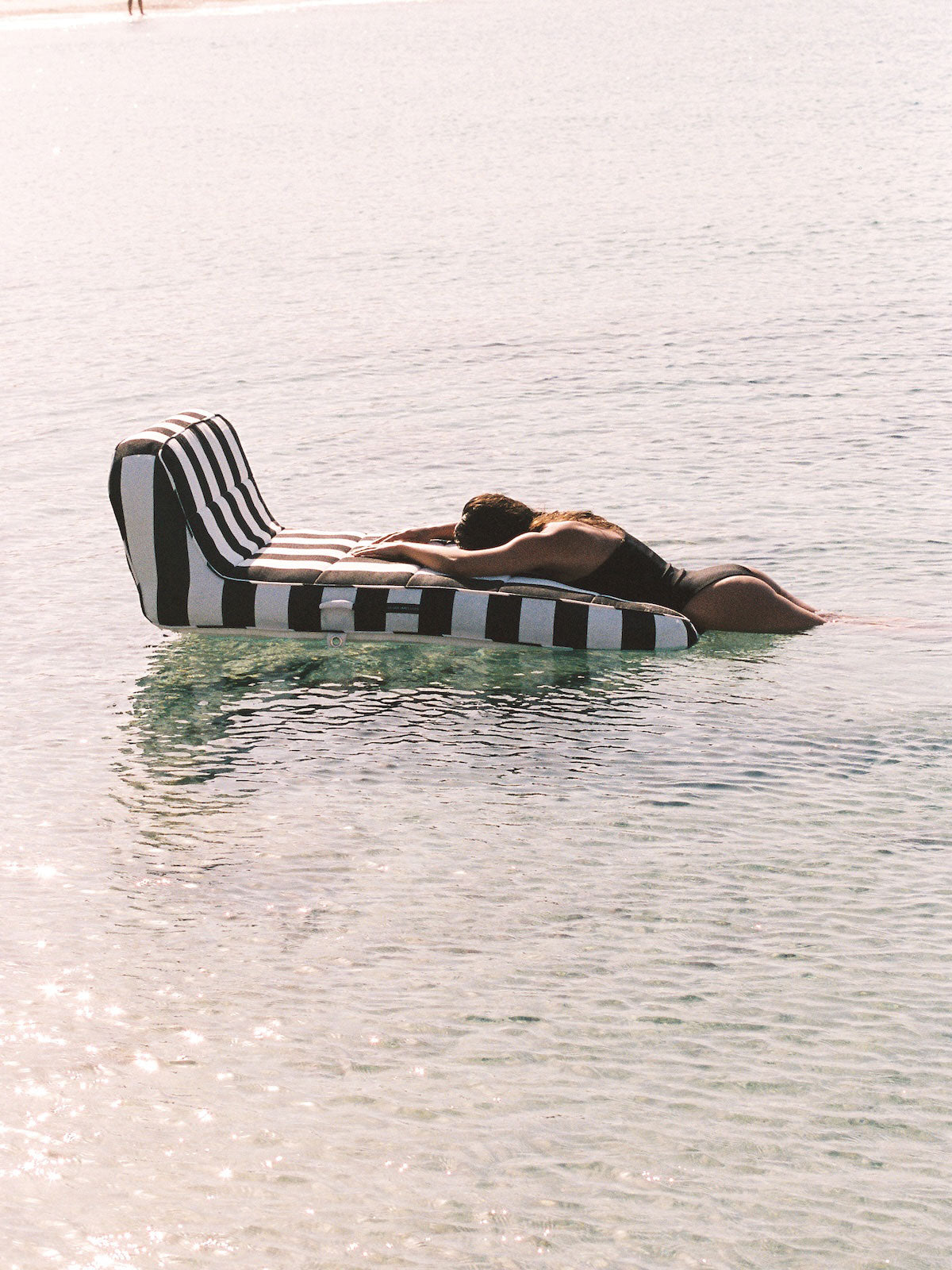 A woman lying on the end of a luxury pool float in the ocean.