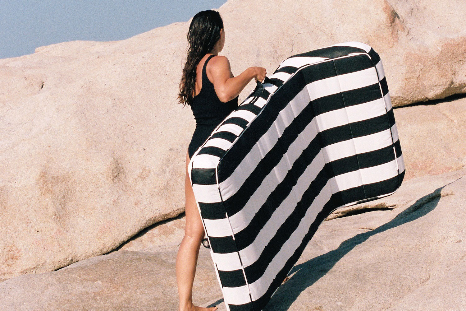 A women carrying a luxury black and white pool float across rocks.