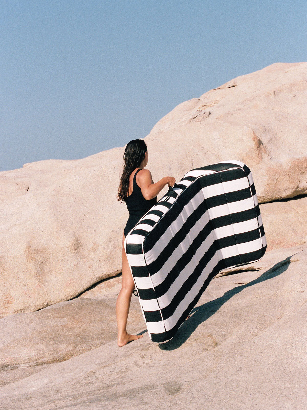 A women carrying a luxury black and white pool float across rocks.