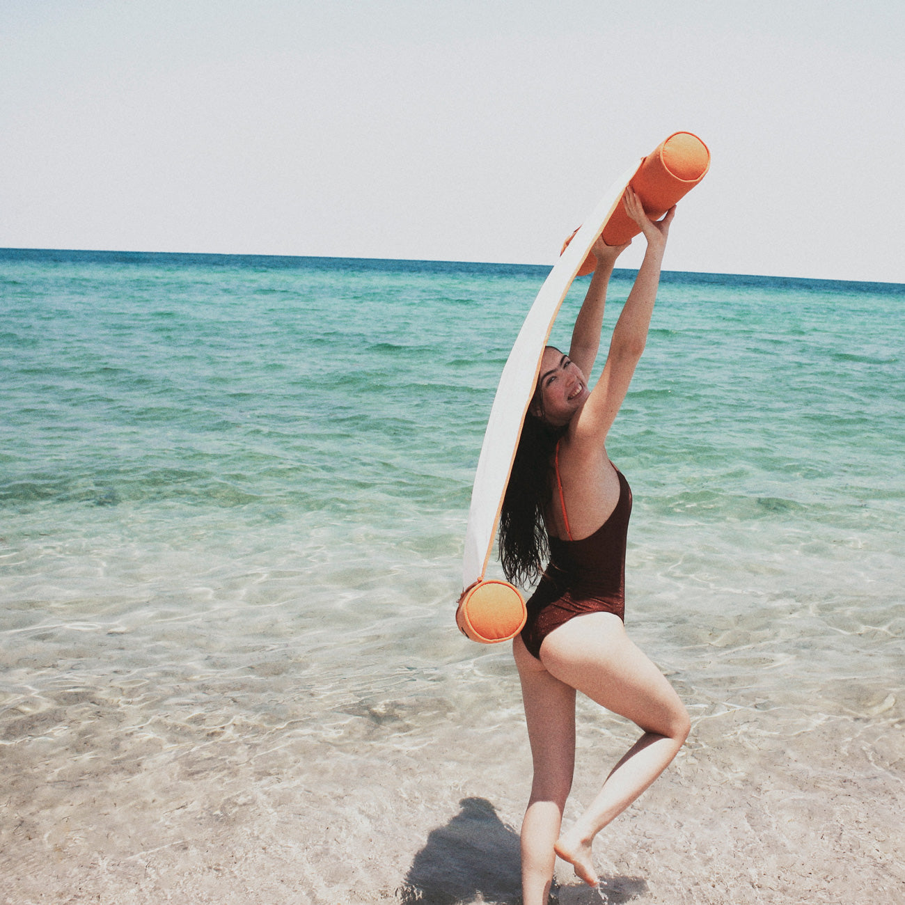 A women on a beach dragging a luxury pool float in the wind.