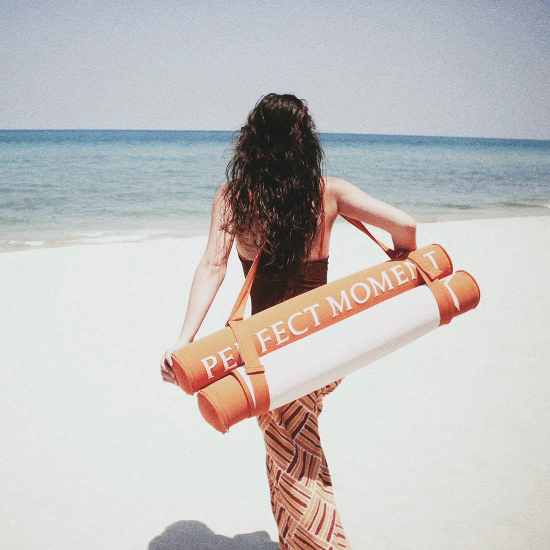 A women on a beach carrying a luxury pool float to the sea.