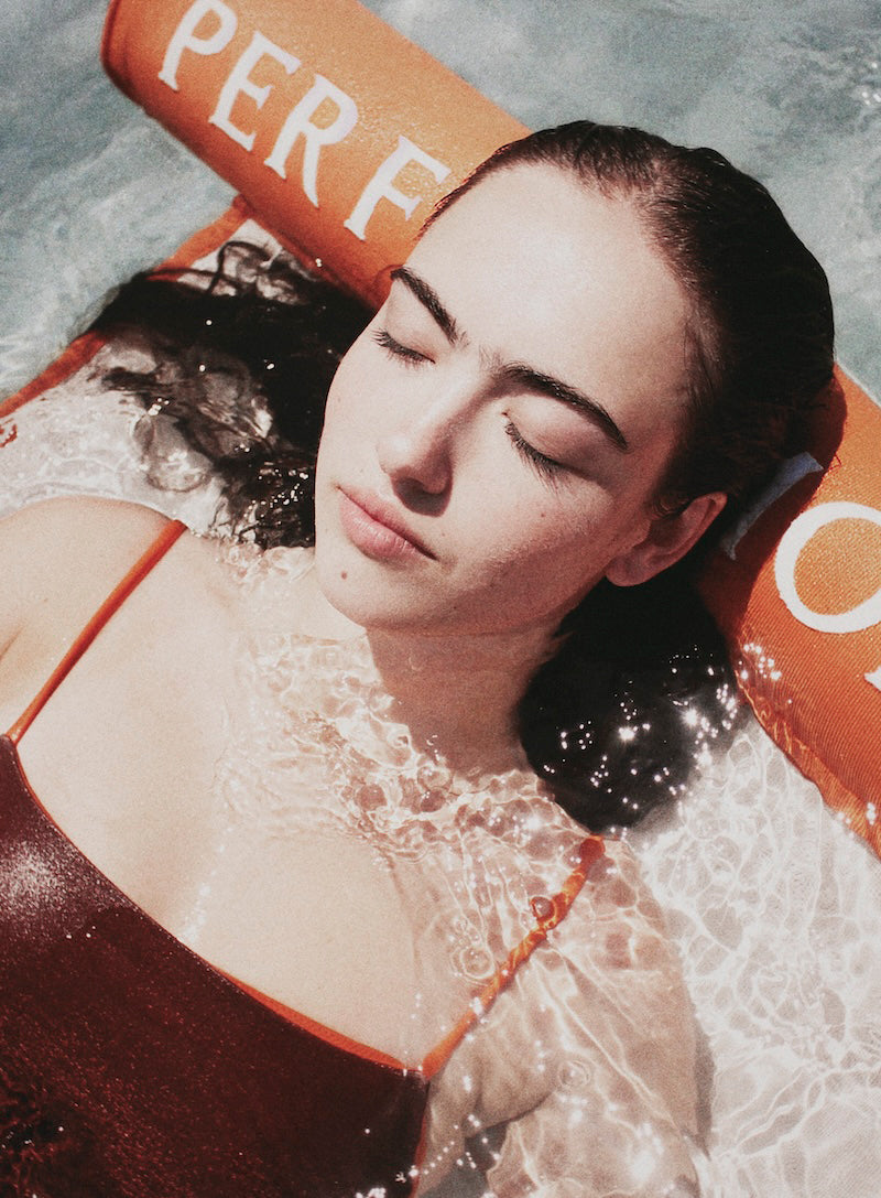 A women in water, close up of her face relaxing on a luxury pool float.