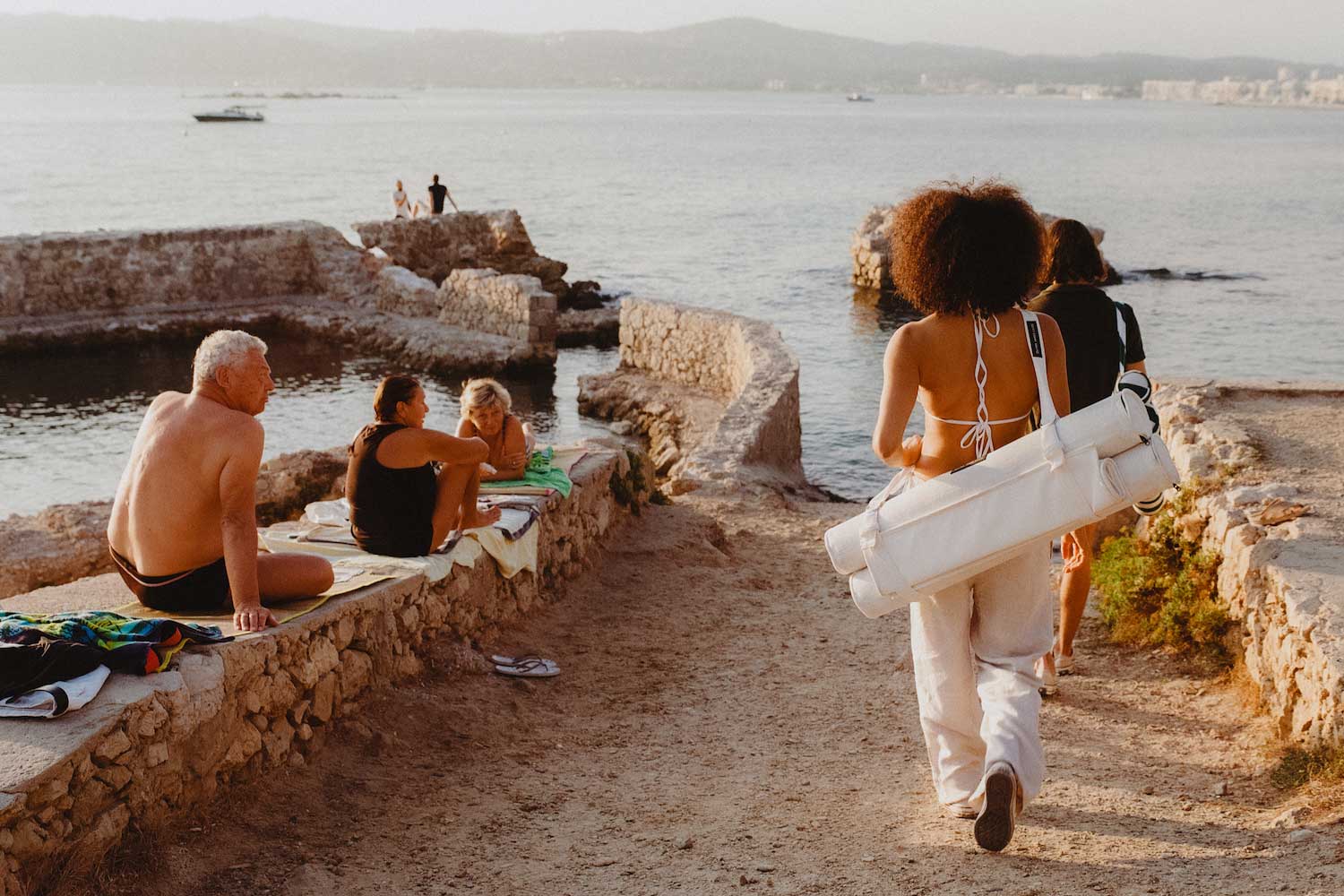 Une femme marchant vers l'océan avec un flotteur de plage pour adultes attaché à son dos et des étrangers qui la regardent.