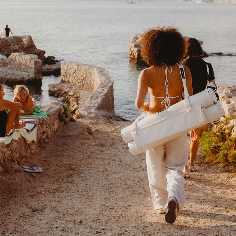 A women walking to the beach with a luxury floating pool hammock strapped to her back