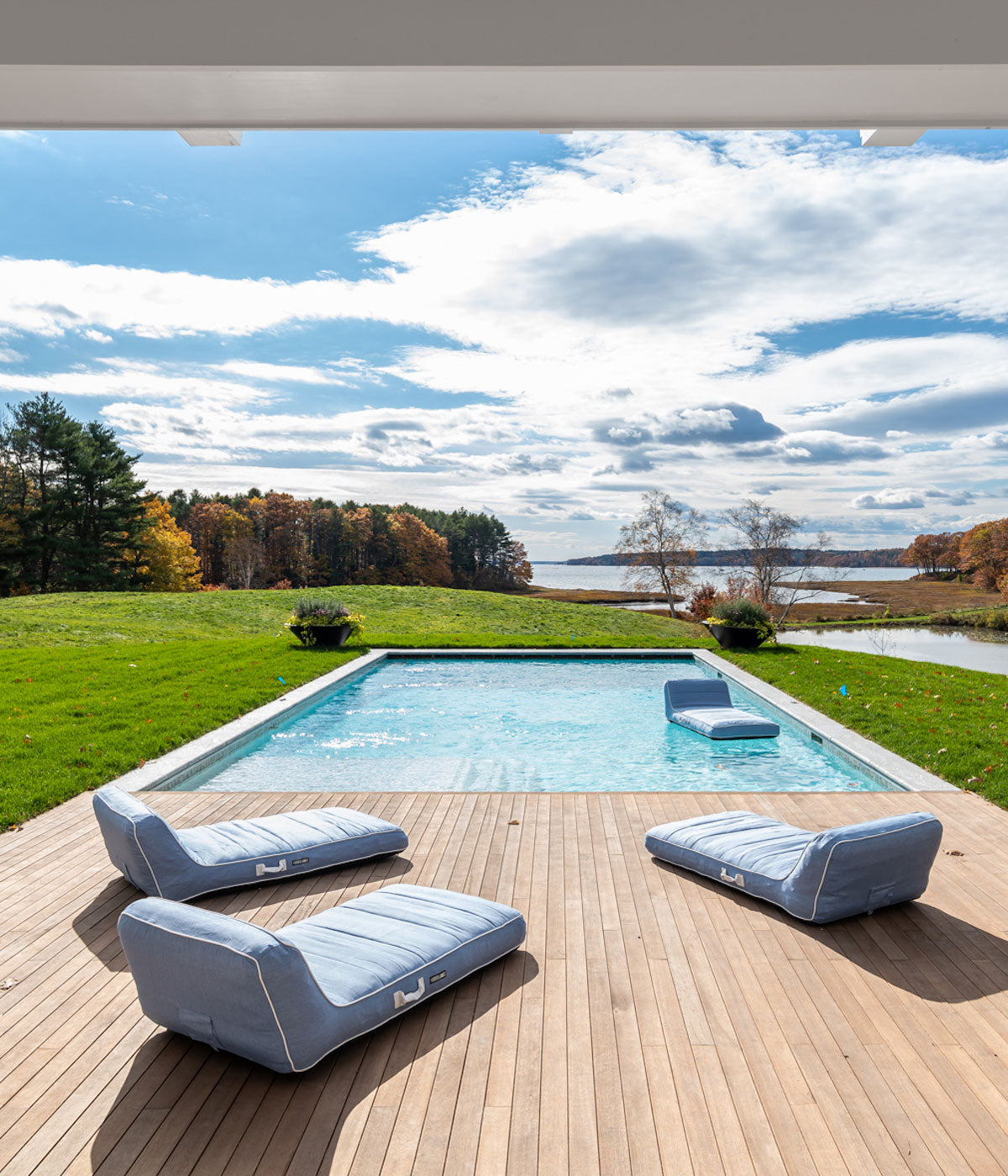 Four luxury pool floats on a wooden deck and floating inside a swimming pool with a background of rolling hills and lakes.