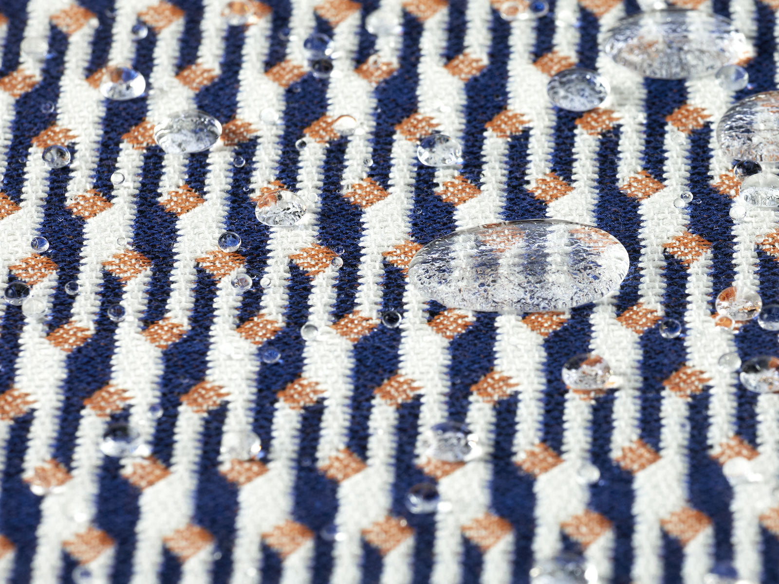 A waterproof outdoor fabric in blue, white and orange colors with several water droplets in frame. 
