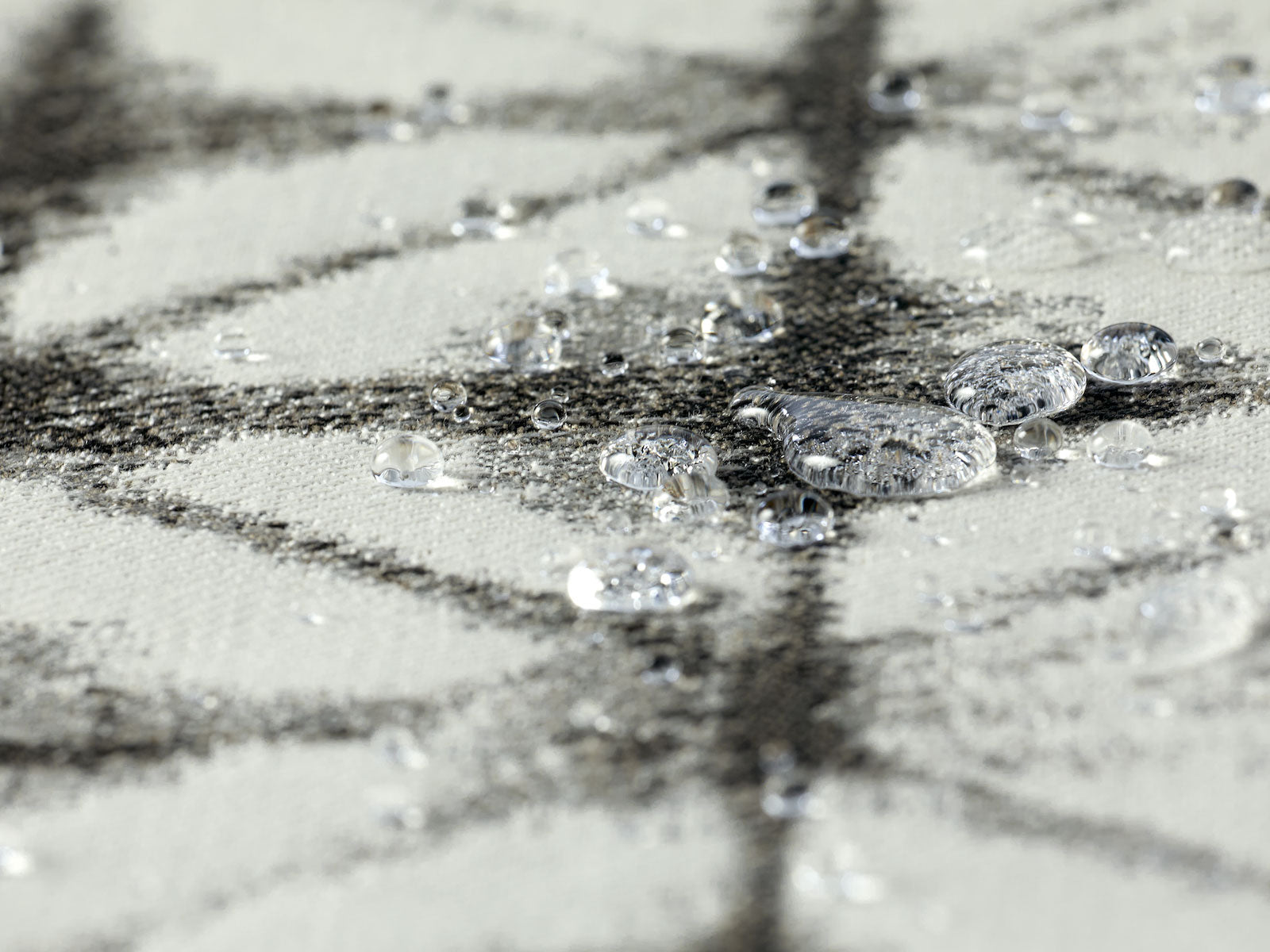 A waterproof outdoor fabric in grey and white colors with several water droplets in frame. 