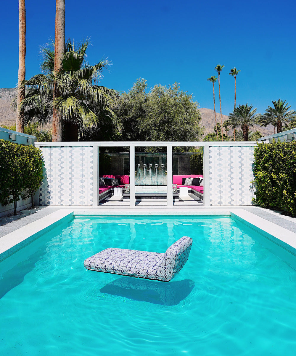 A blue and white patterned luxury pool float floating in the middle of a Palm Springs Mid Century Modern swimming pool.