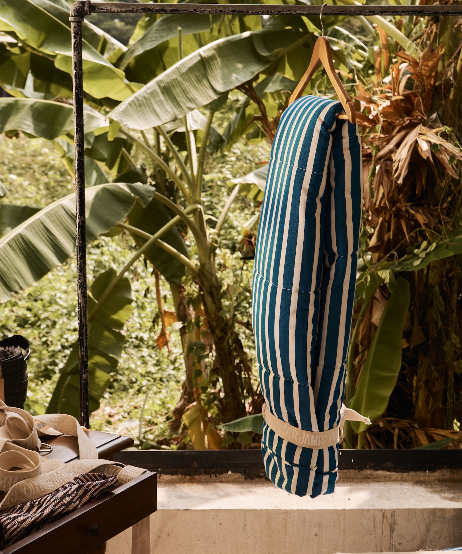 Une housse de flotteur de piscine pour adultes suspendue à un porte-tout, avec des plantes tropicales en arrière-plan et des éléments de lilo de luxe au premier plan.
