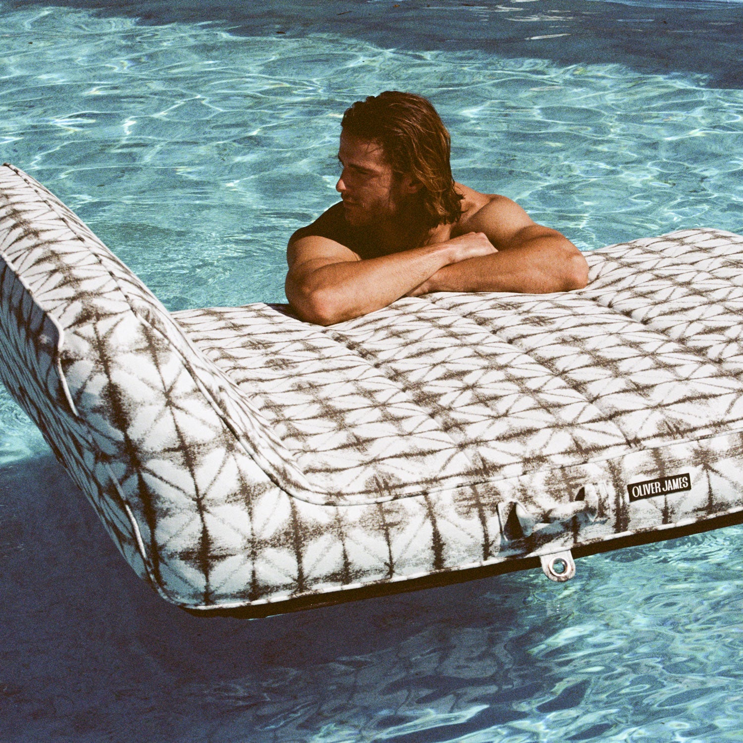 A mean leaning on a grey and white double pool float lounger for adults in a swimming pool.