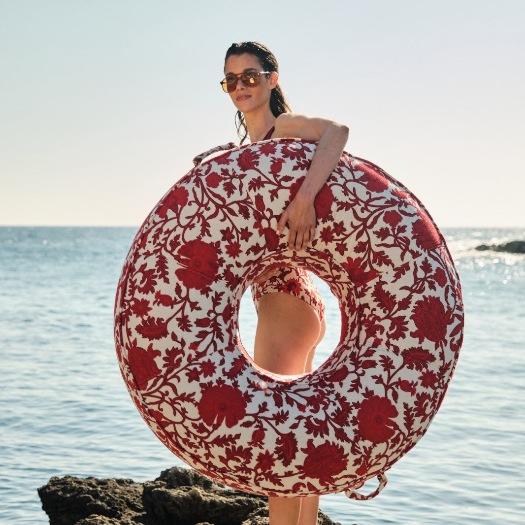 A woman holding a luxury pool float upholstered in red and white fabric.