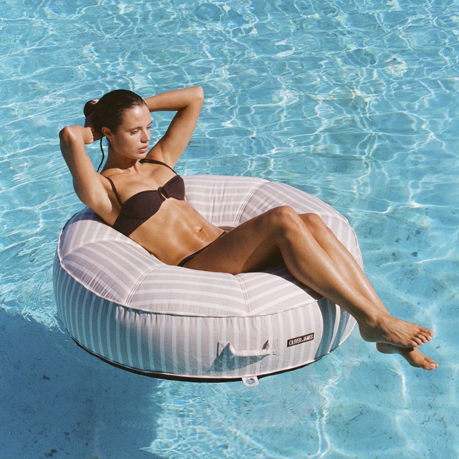 Une femme sur un flotteur de piscine rayé blanc et beige Bague flottant dans une piscine.