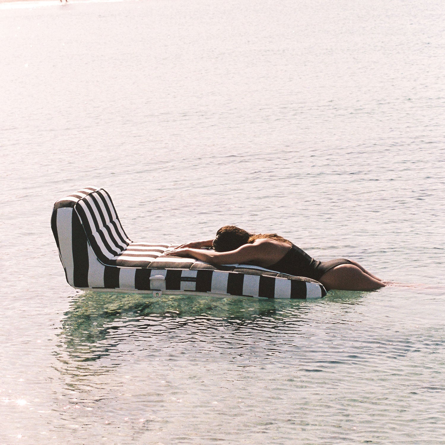 A women lying on the end of a black and white luxury pool float in the ocean.