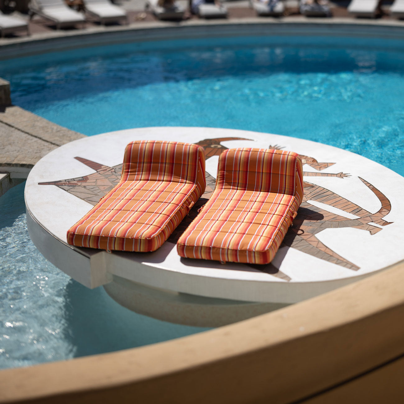 Two orange and white striped pool float loungers for adults sitting on a podium next to a swimming pool.