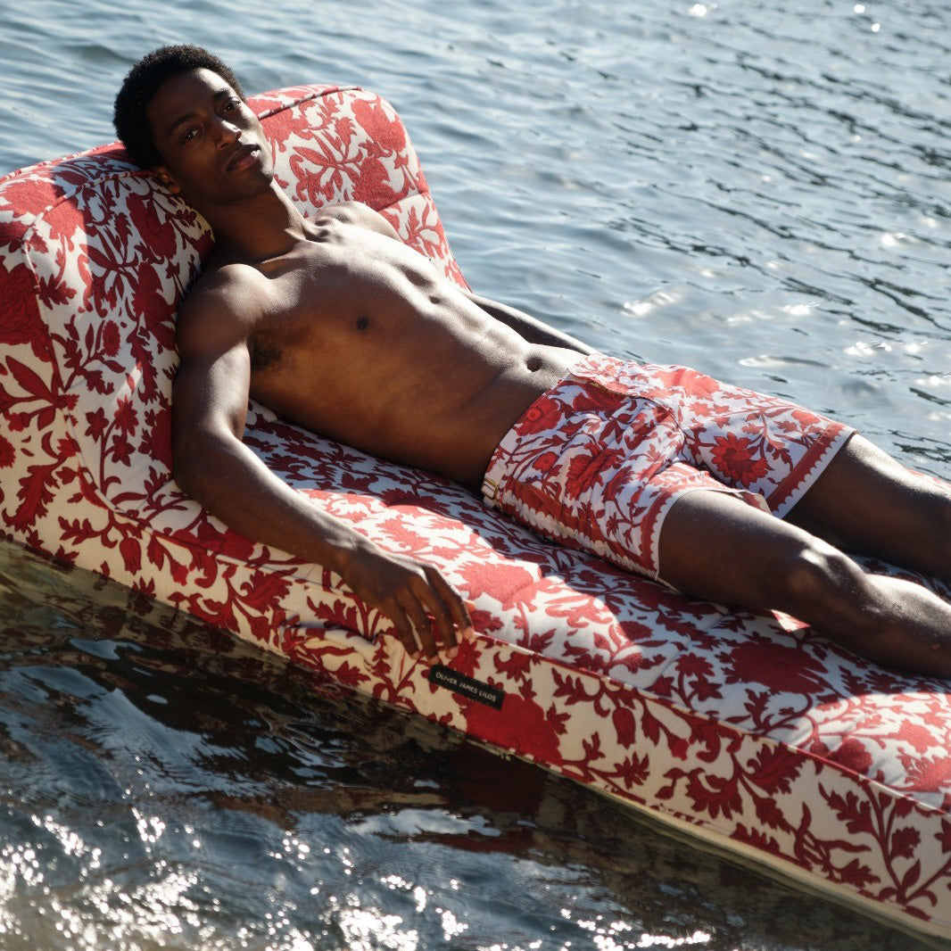 A man floating on a luxury pool float upholstered in red and white fabric.