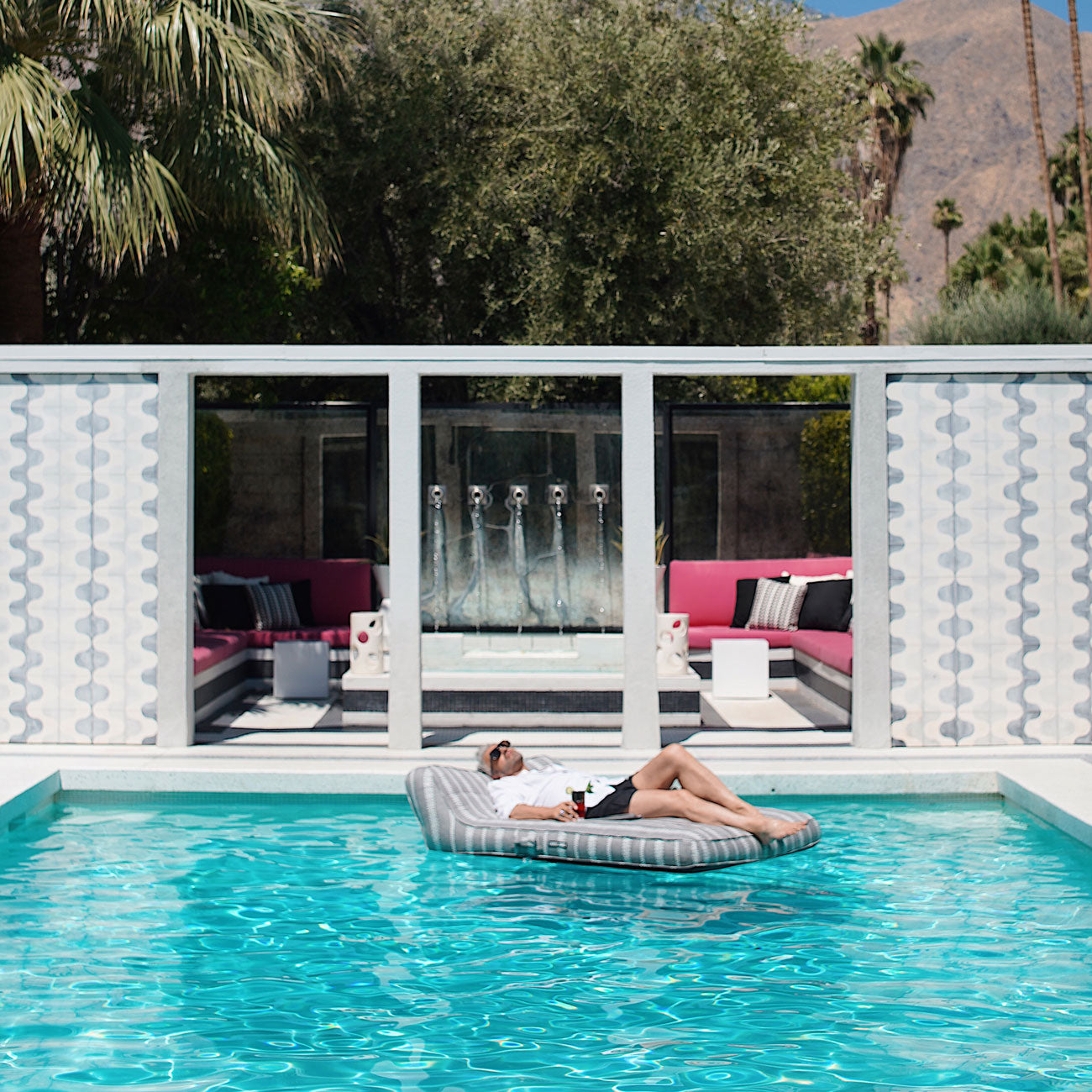 A grey and white striped pool float lounger for adults floating in a swimming pool with man relaxing on it.