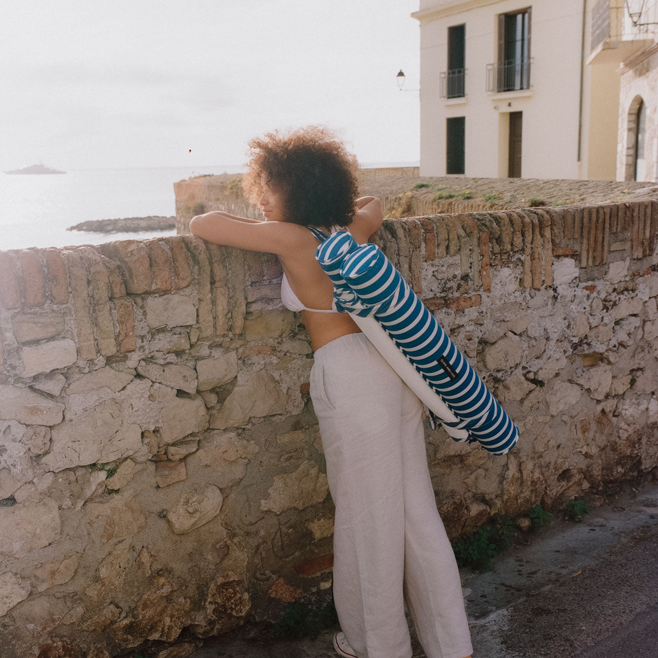 Une femme appuyée sur un mur au bord de la mer avec un jouet de piscine pour adultes sur le dos.