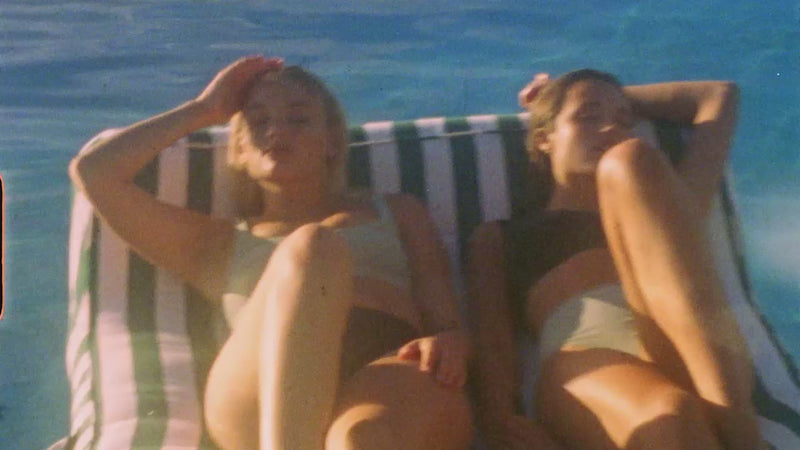 Deux femmes allongées sur un double flotteur de luxe dans une piscine, montées à l'aide de clips vidéo super huit et numériques.