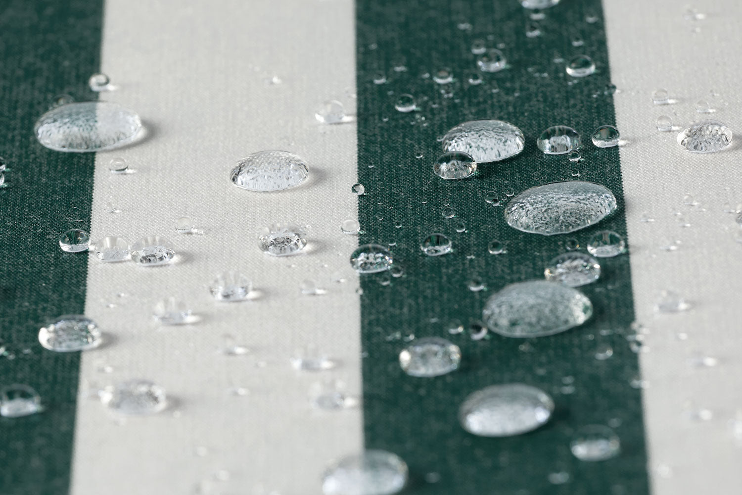 A waterproof outdoor fabric in a green and white bar stripe with several water droplets in frame. 